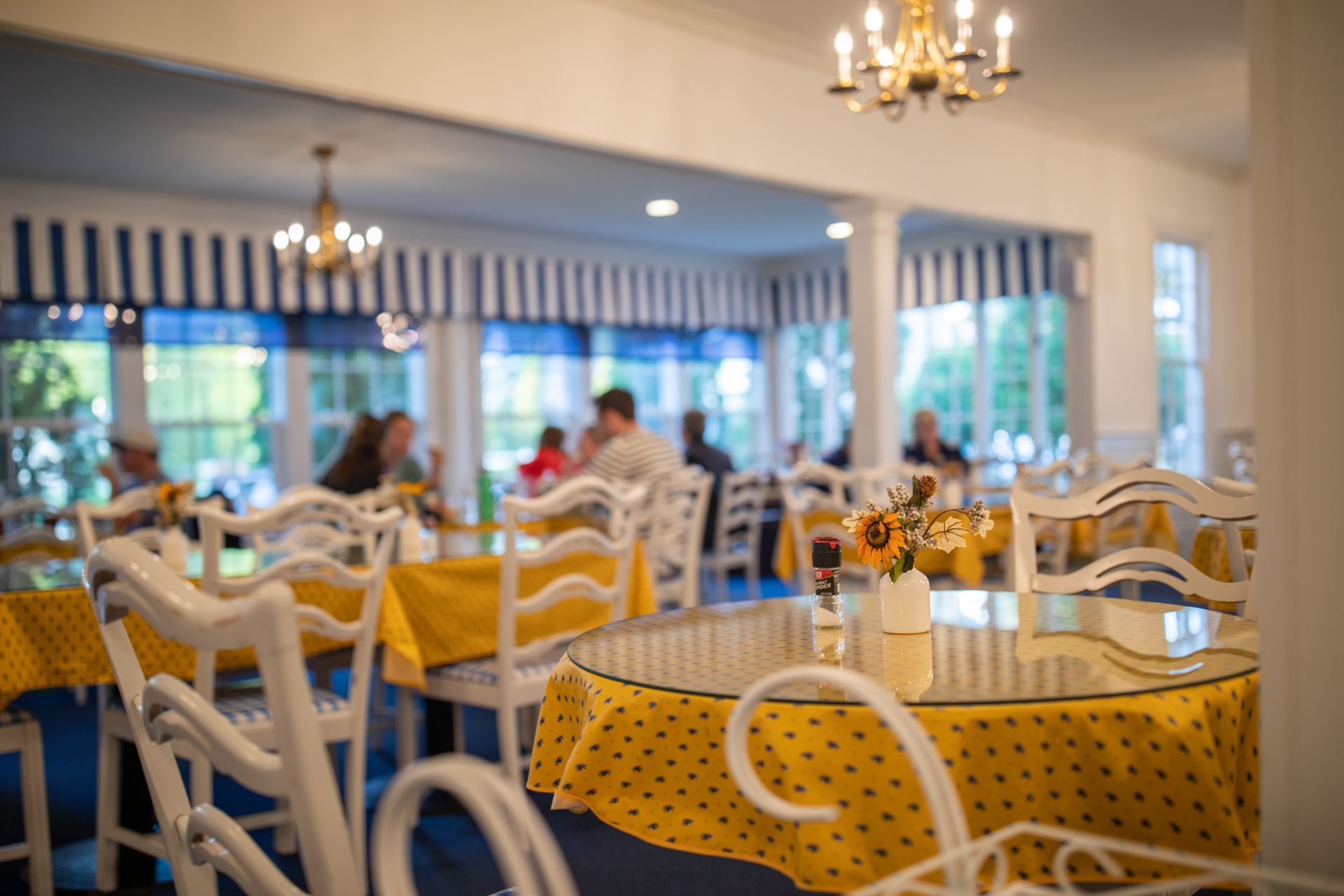 Bright dining room with yellow polka-dot tablecloths, white chairs, and chandeliers near large windows