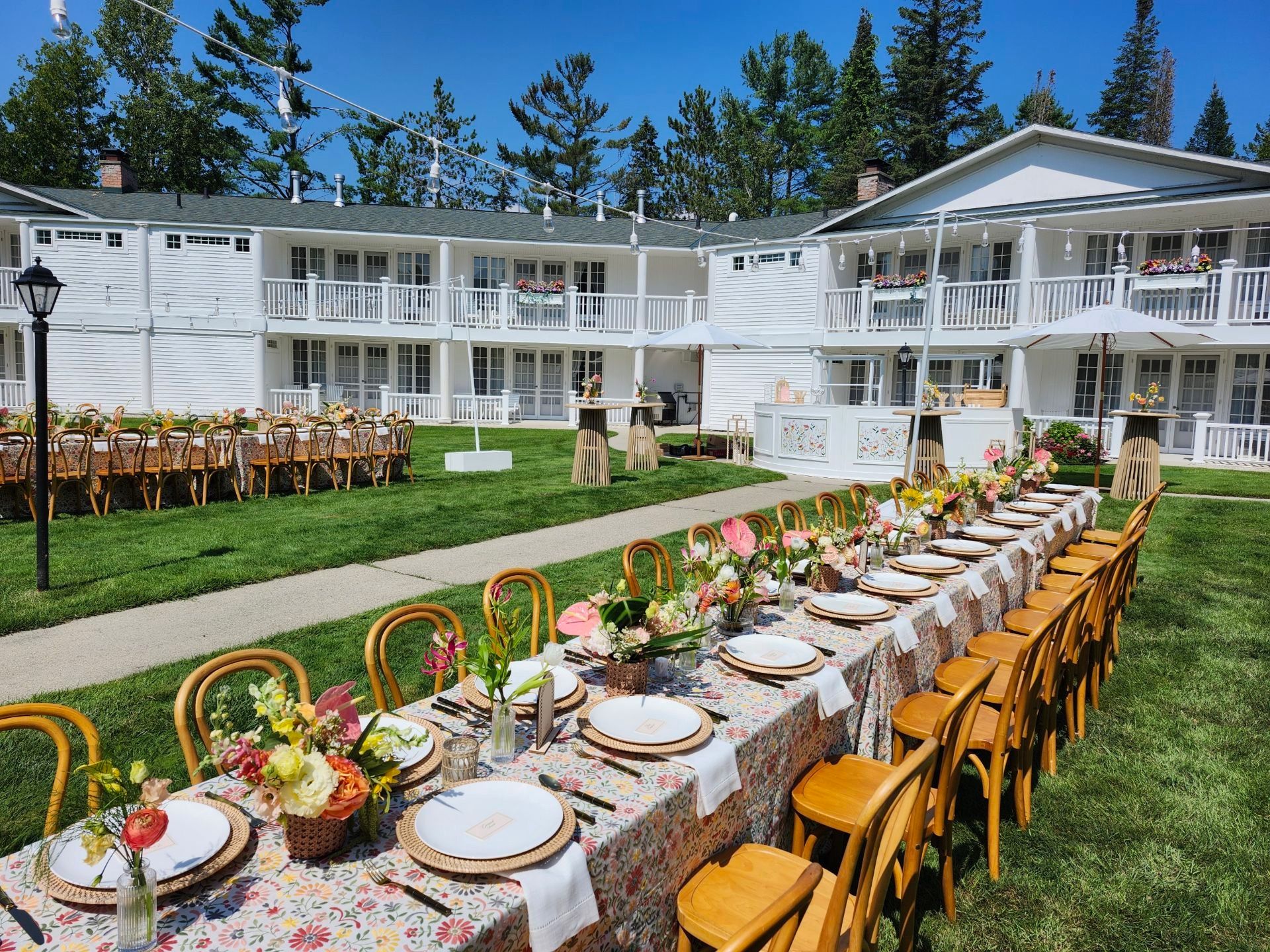 Elegant outdoor dining table set on a lawn in front of a white resort building with balconies and flowers