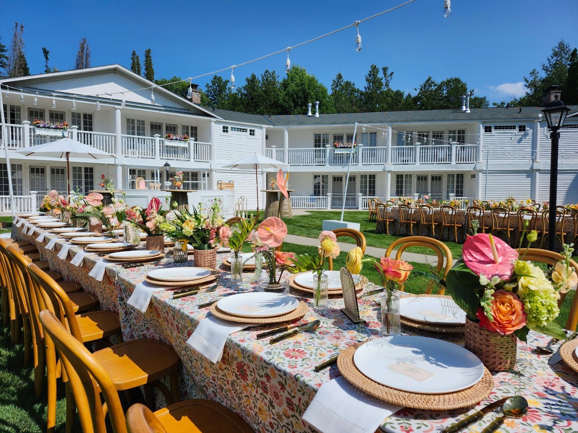 Long outdoor banquet table with flowers and place settings in a sunny courtyard outside white buildings