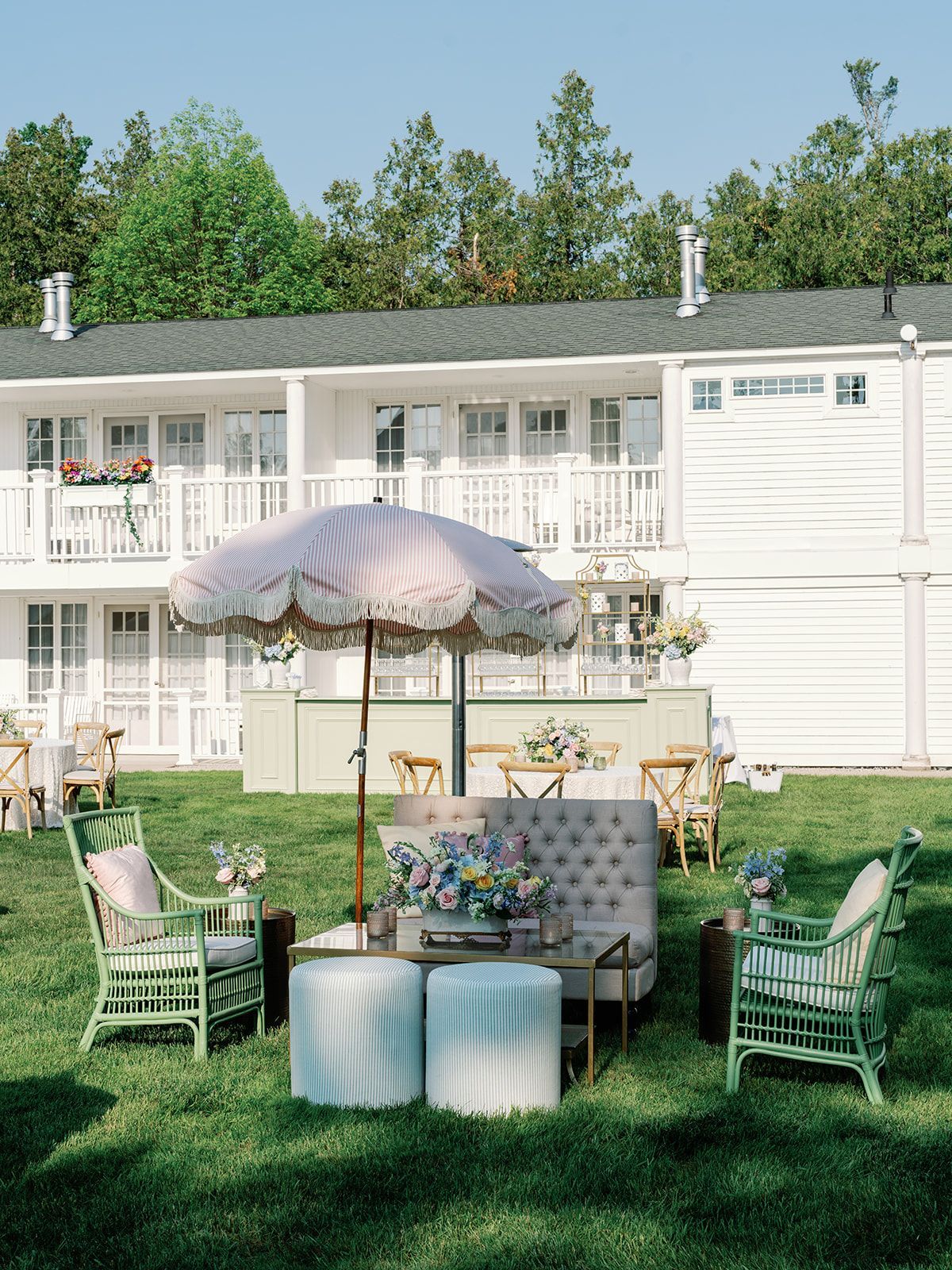 Outdoor garden tea setup with pastel chairs, umbrella, and floral table in front of a white motel building