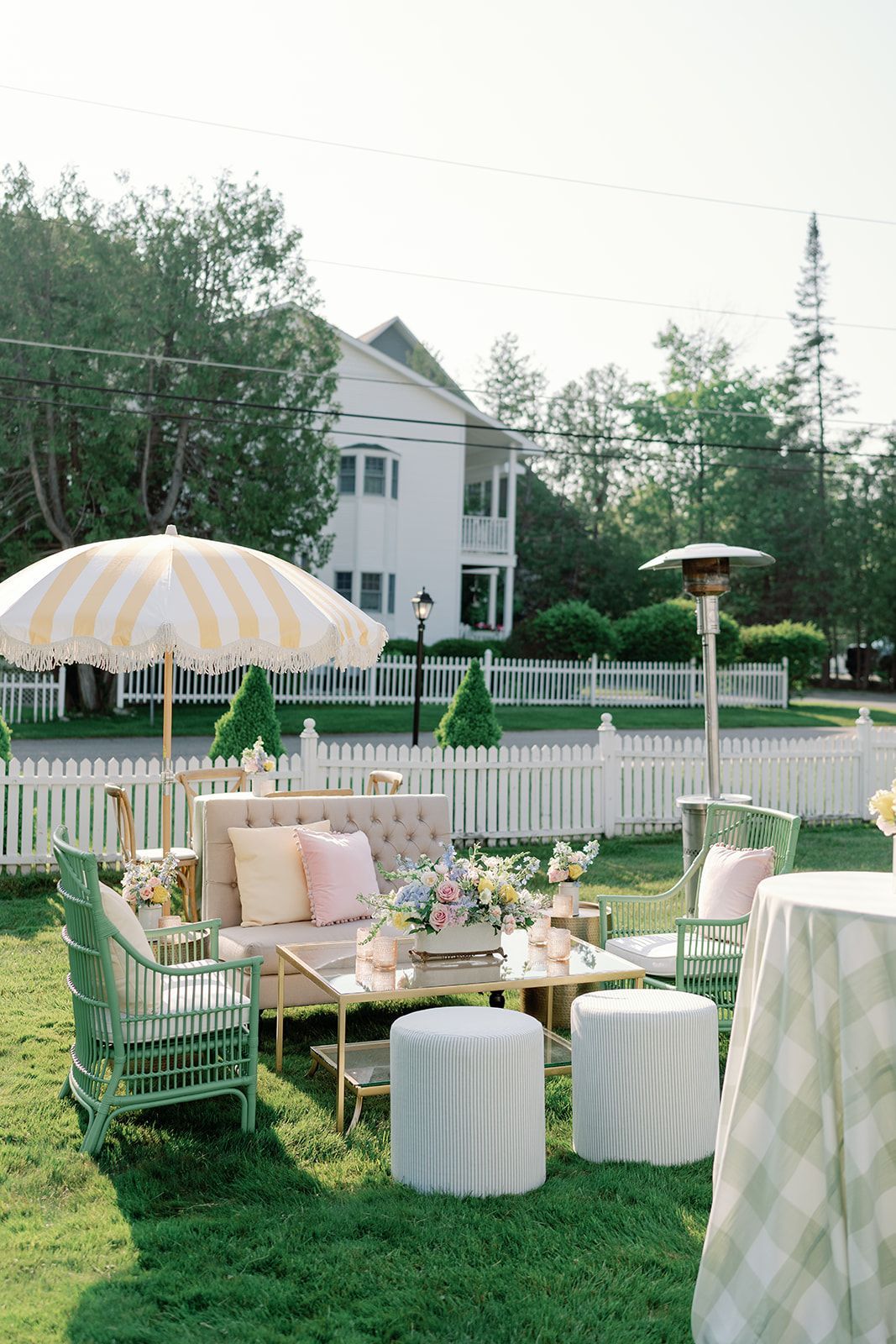 Pastel outdoor picnic setup with striped umbrellas, cushions, and a white house in the background