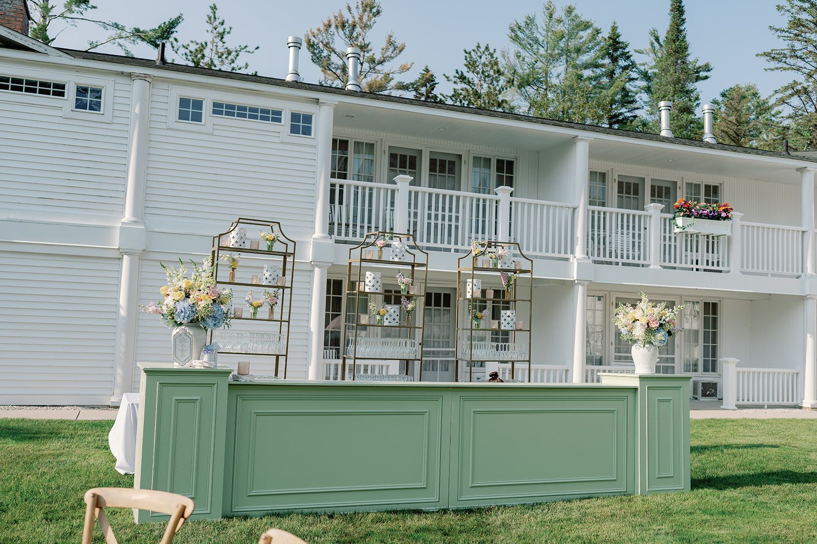 White two-story house with a mint-green outdoor bar and floral arrangements on a lawn