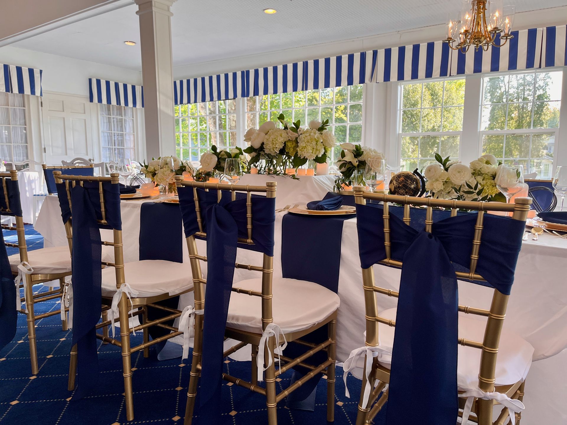 Elegant event dining room with blue-and-white decor, gold chairs, floral centerpieces, and large windows