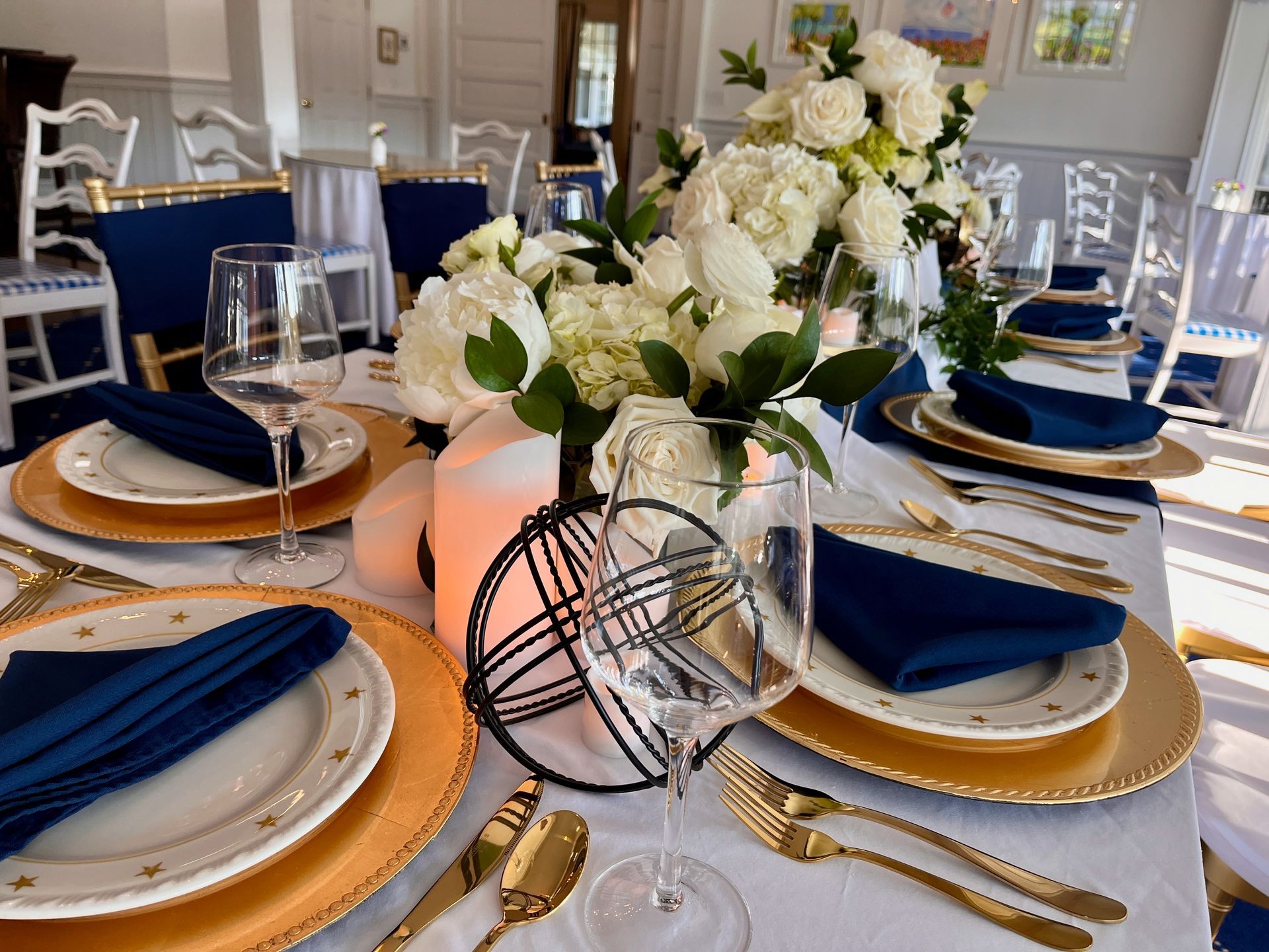 Elegant banquet table with navy napkins, gold-rimmed plates, and white floral centerpiece in a bright dining room