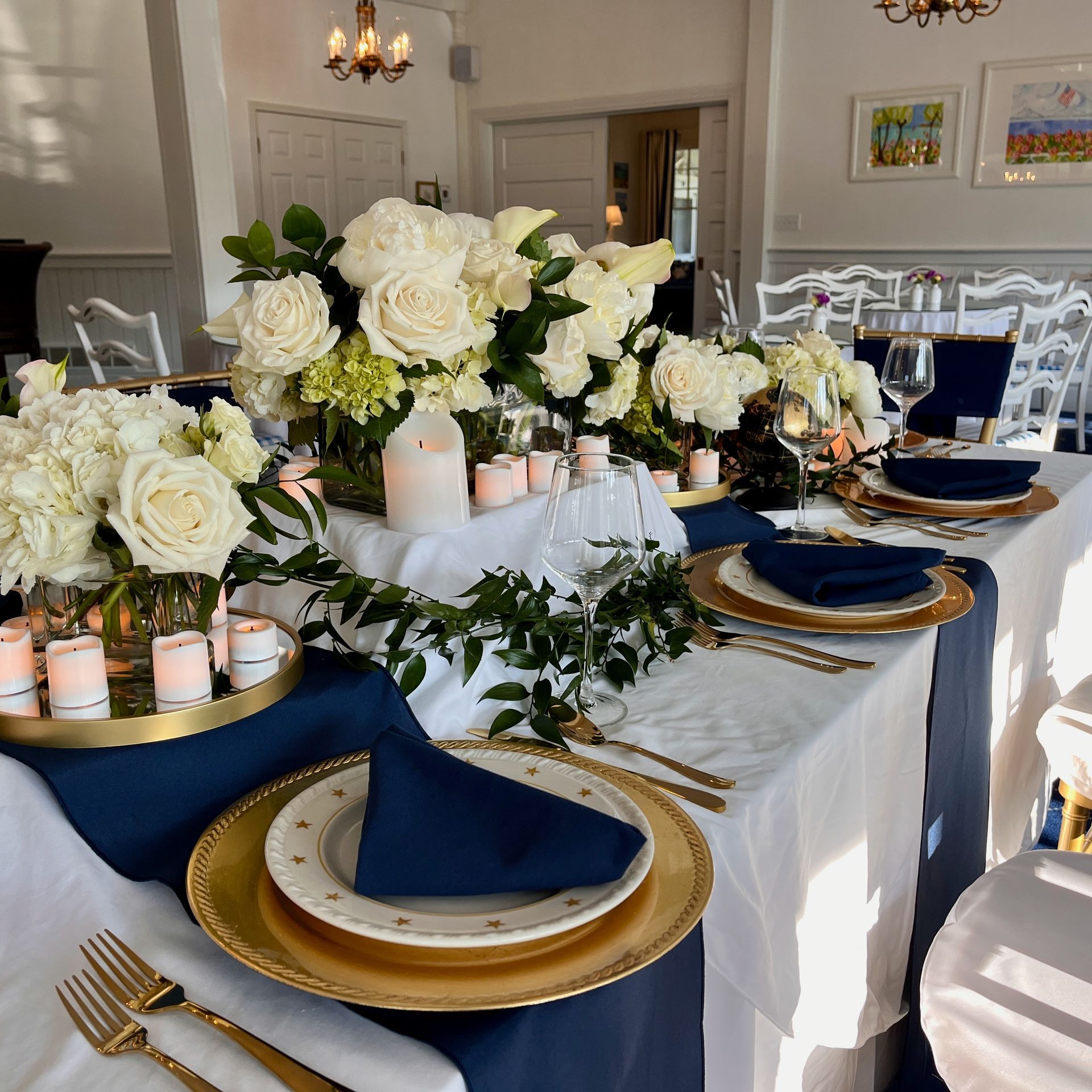 Elegant banquet table set with white flowers, gold chargers, navy napkins, and candle centerpieces