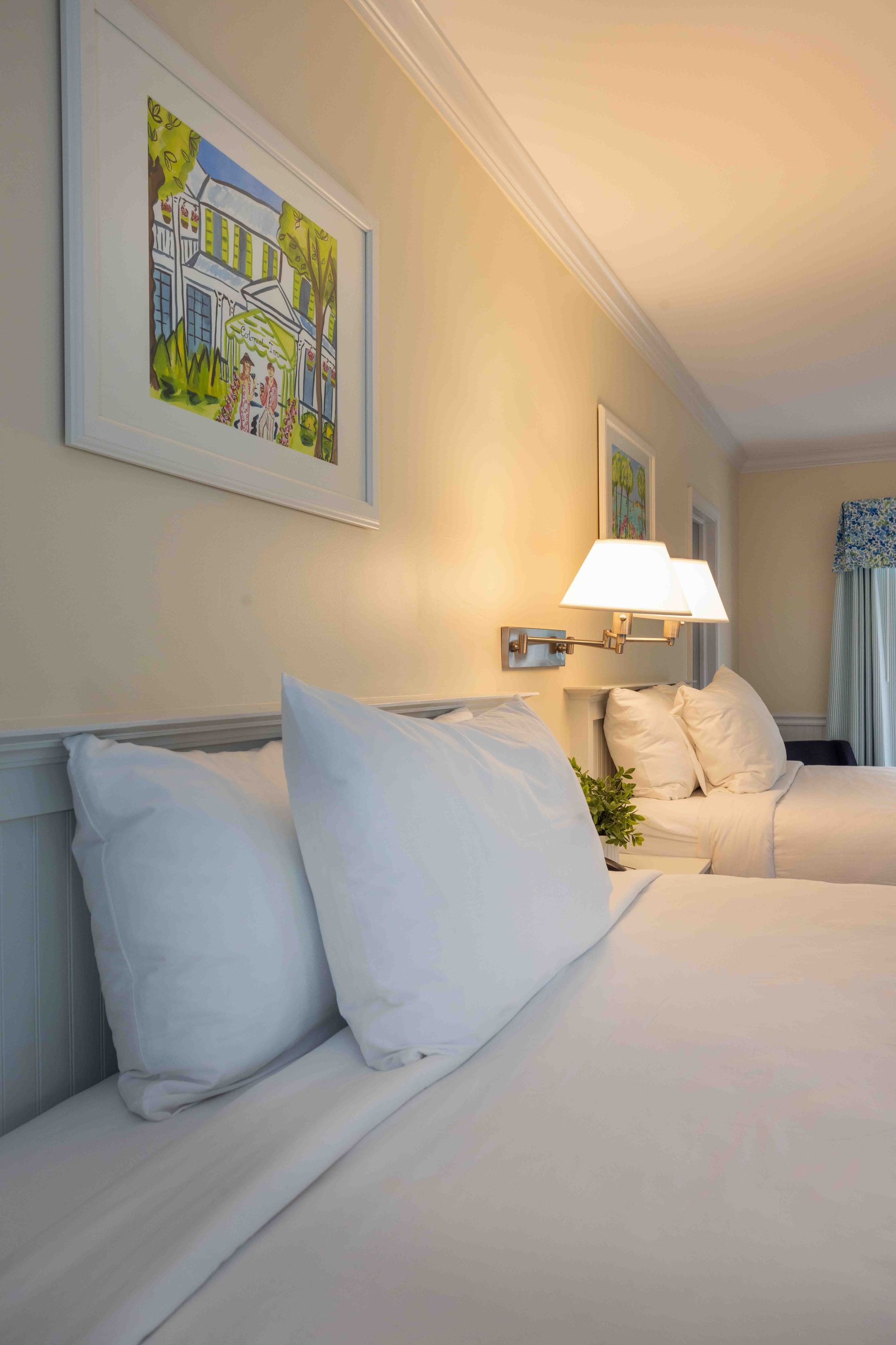 Neatly made bed with white pillows in a softly lit hotel room with wall art and lamps