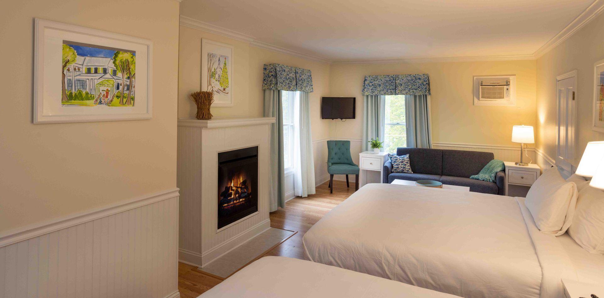 Cozy bedroom with a fireplace, king bed, two blue chairs, and warm lamp lighting