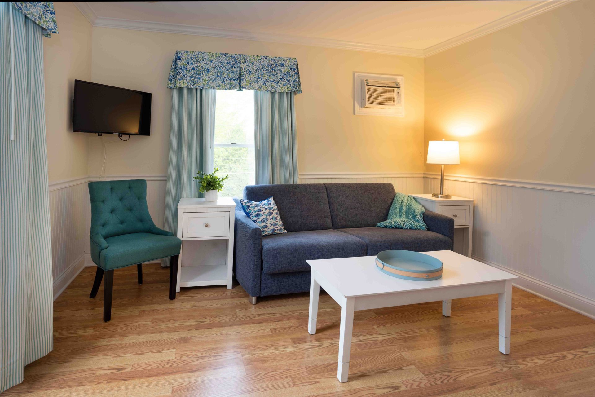 Cozy living room with blue sofa, teal chair, white coffee table, and floor lamp by a window