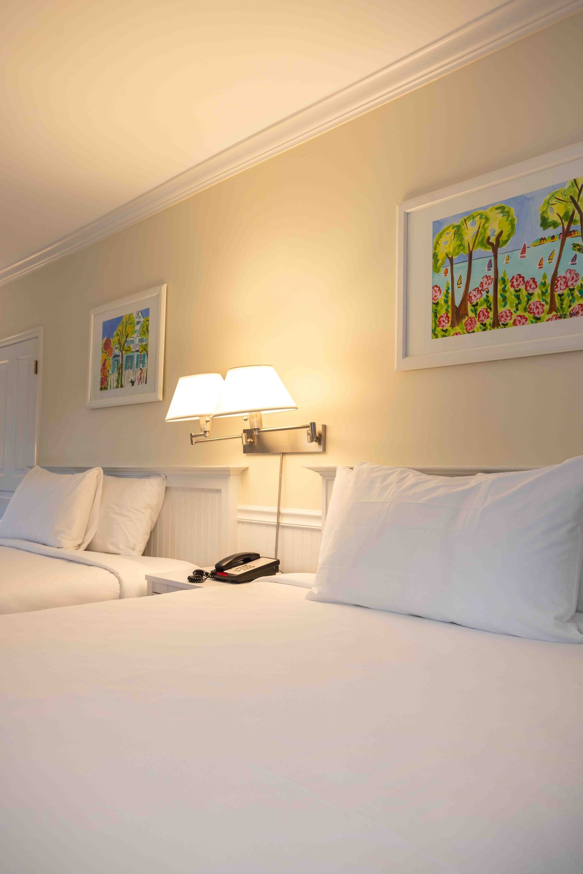 Two white hotel beds with a bedside lamp and framed artwork on a beige wall
