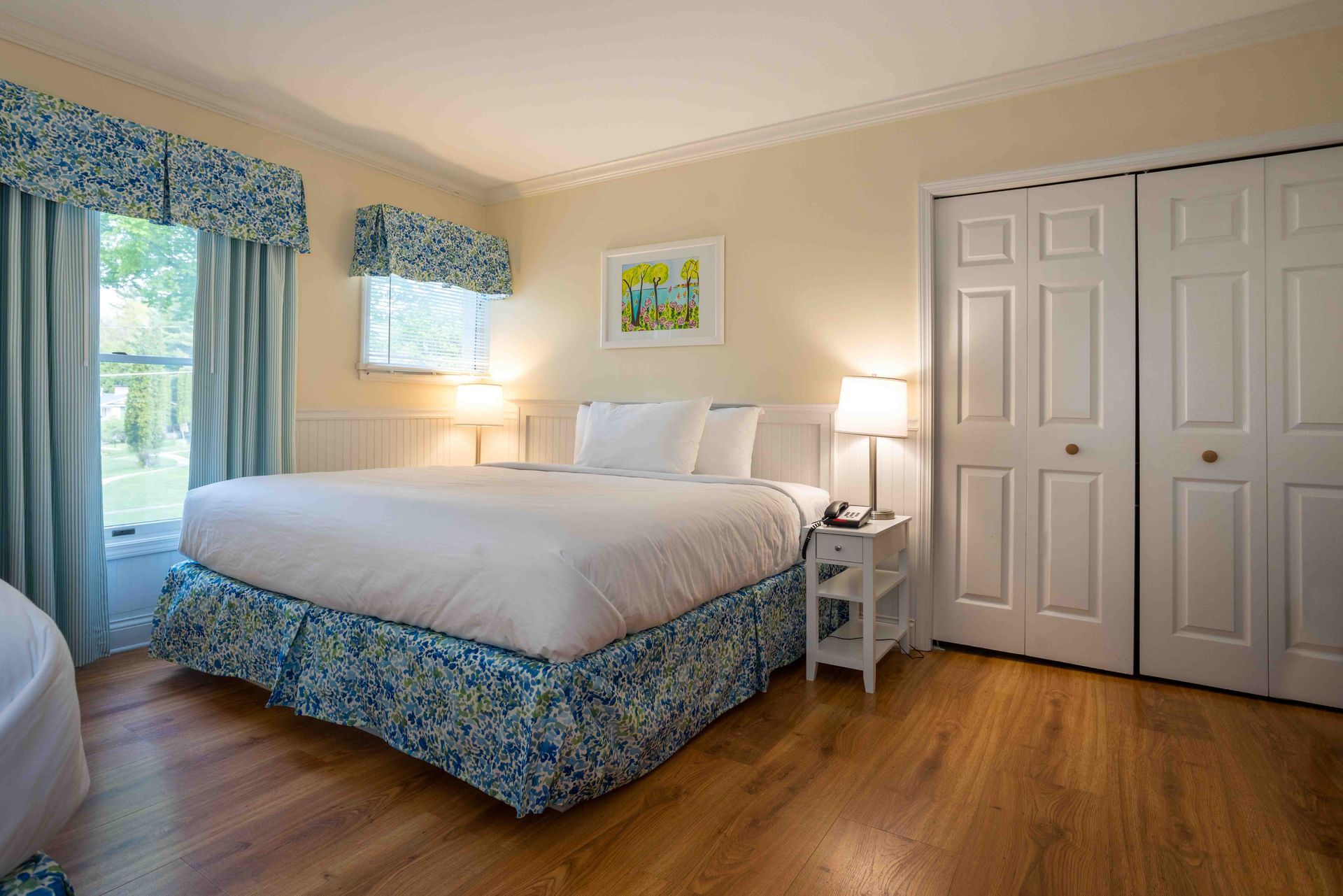 Bright bedroom with a white bed, blue floral accents, nightstands, lamps, and wood floors