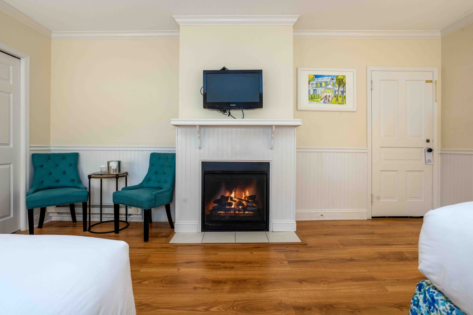 Cozy bedroom with fireplace, wall-mounted TV, teal chairs, and hardwood floor