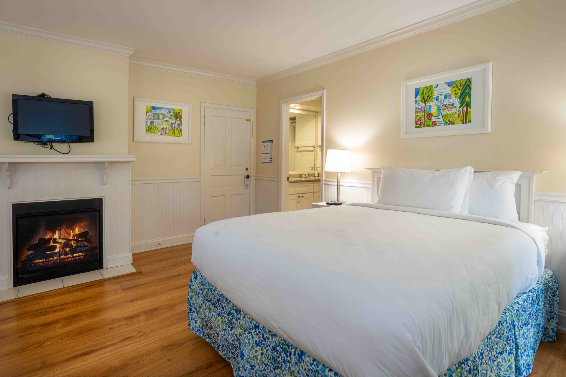 Bright bedroom with white bed, fireplace, TV, and warm wood floors