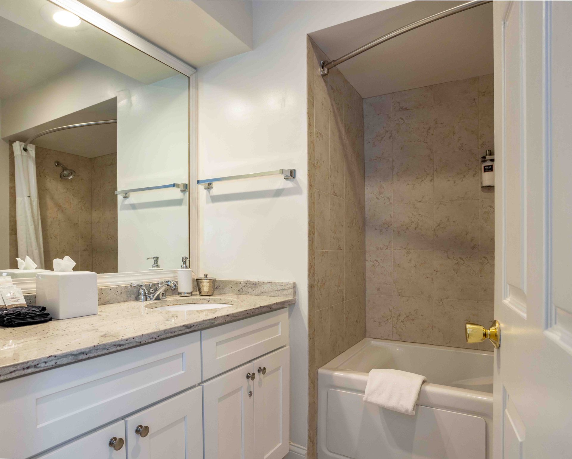 Bright bathroom vanity with mirror and granite counter beside a white tub with a shower curtain rod.