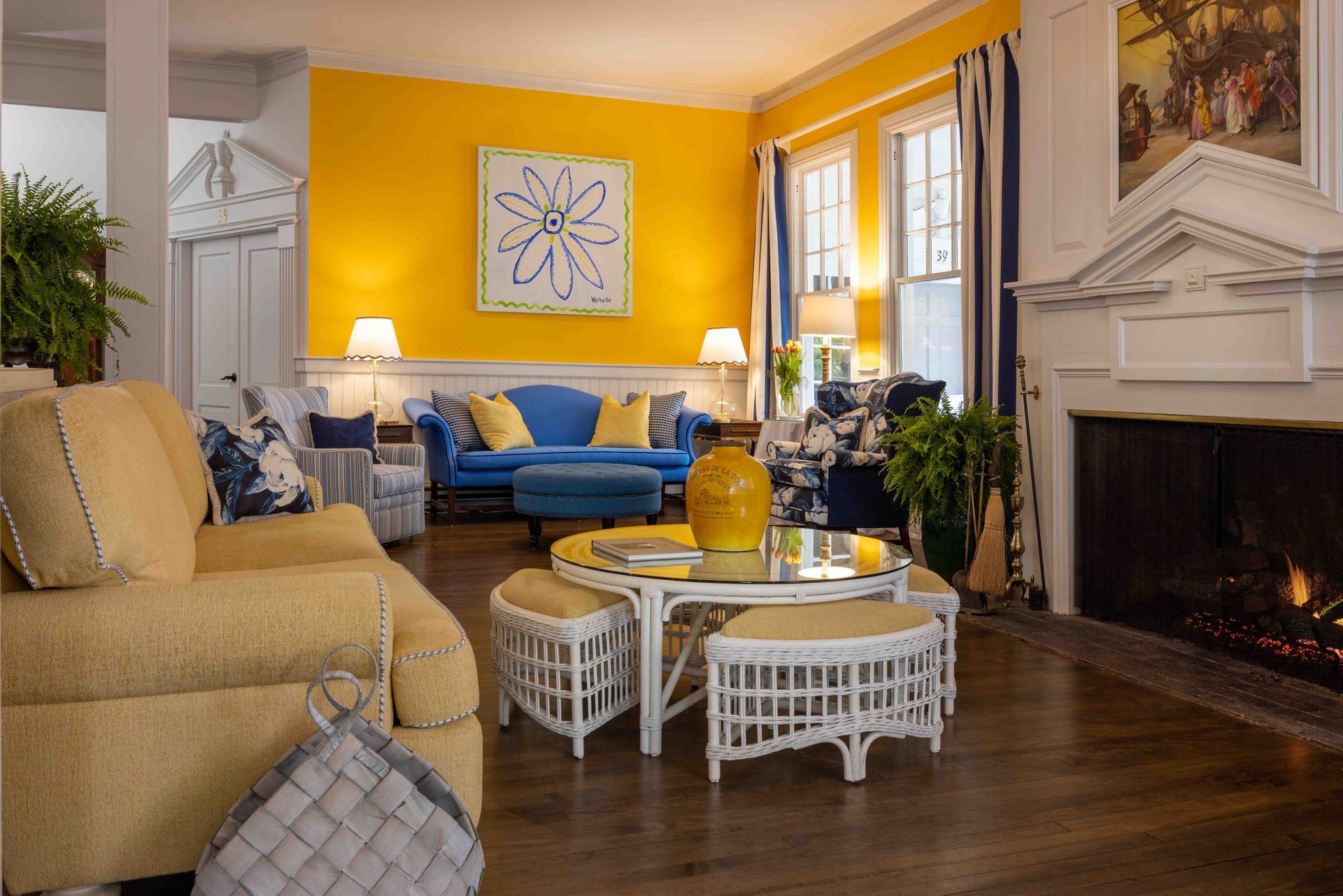 Bright living room with yellow walls, blue sofa, beige chairs, fireplace, and large windows