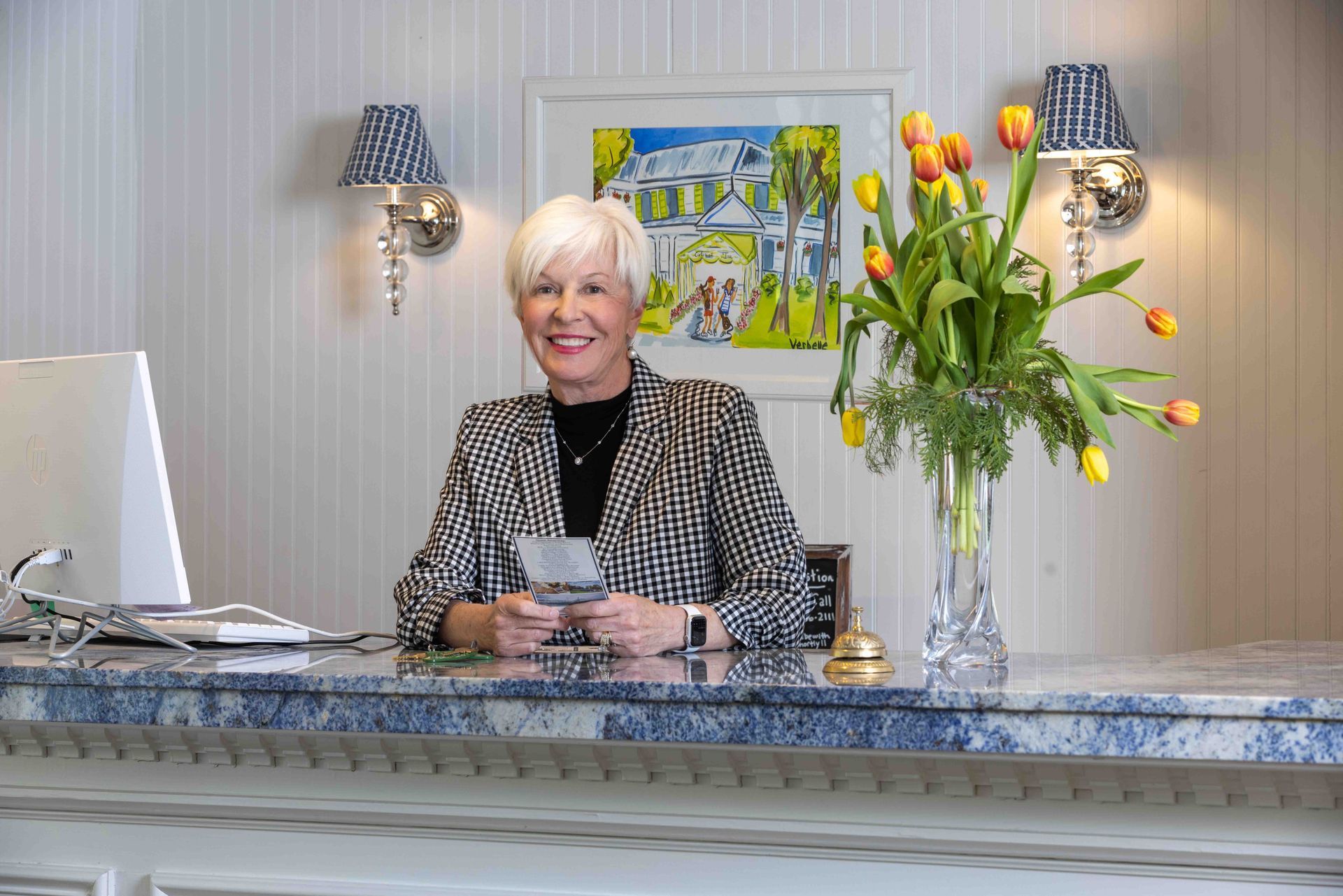 Smiling receptionist behind a blue marble counter with flowers and framed art in a bright lobby