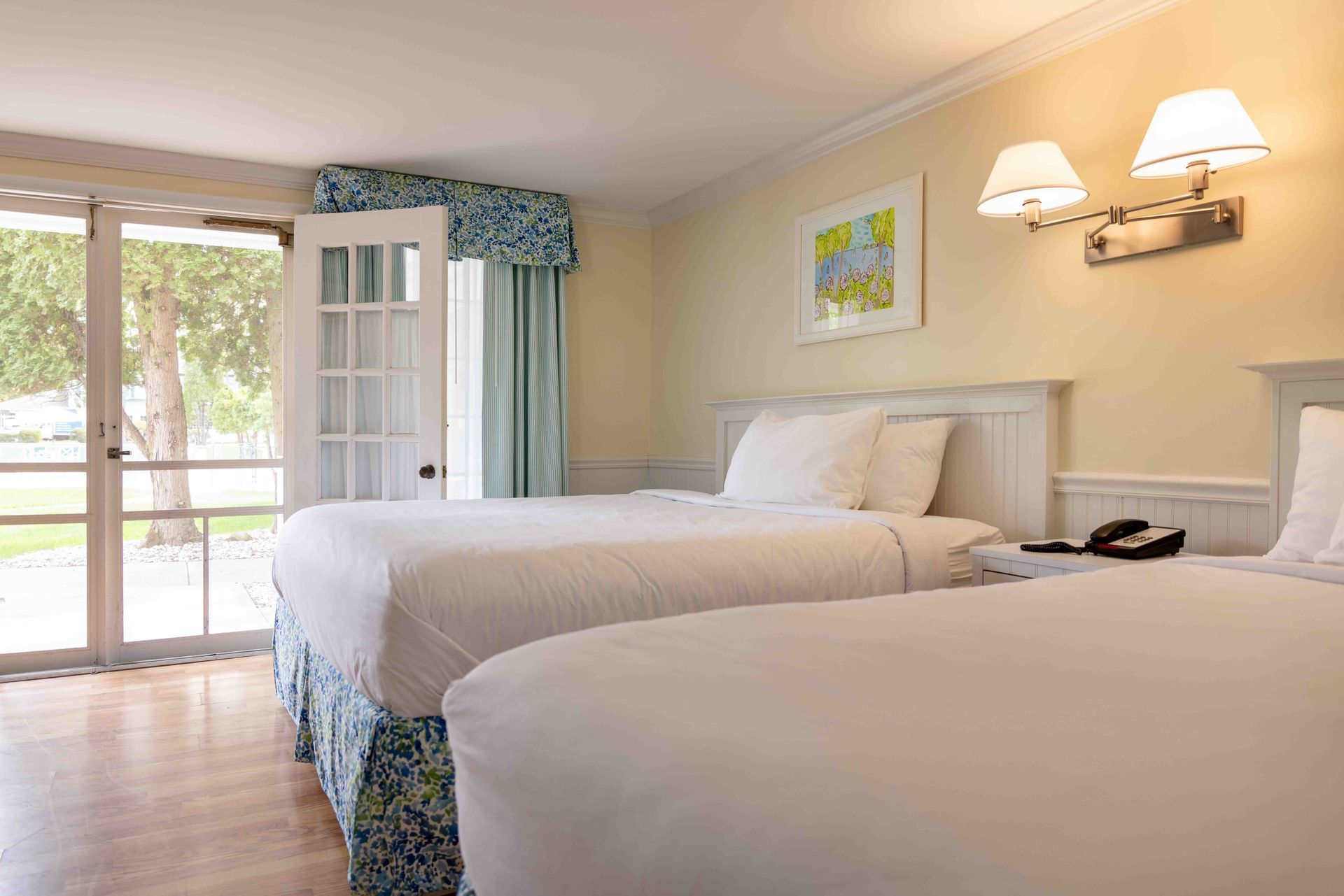 Bright bedroom with two beds, white walls, wall lamps, and a glass door opening to a balcony.