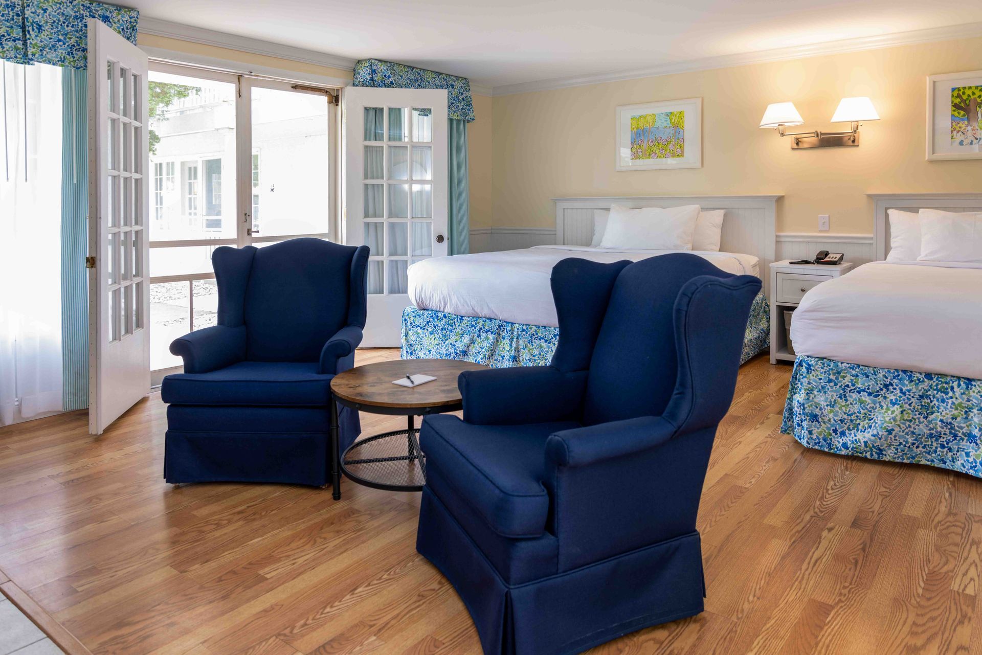 Bright bedroom with blue chairs, twin beds, and open French doors to a balcony.