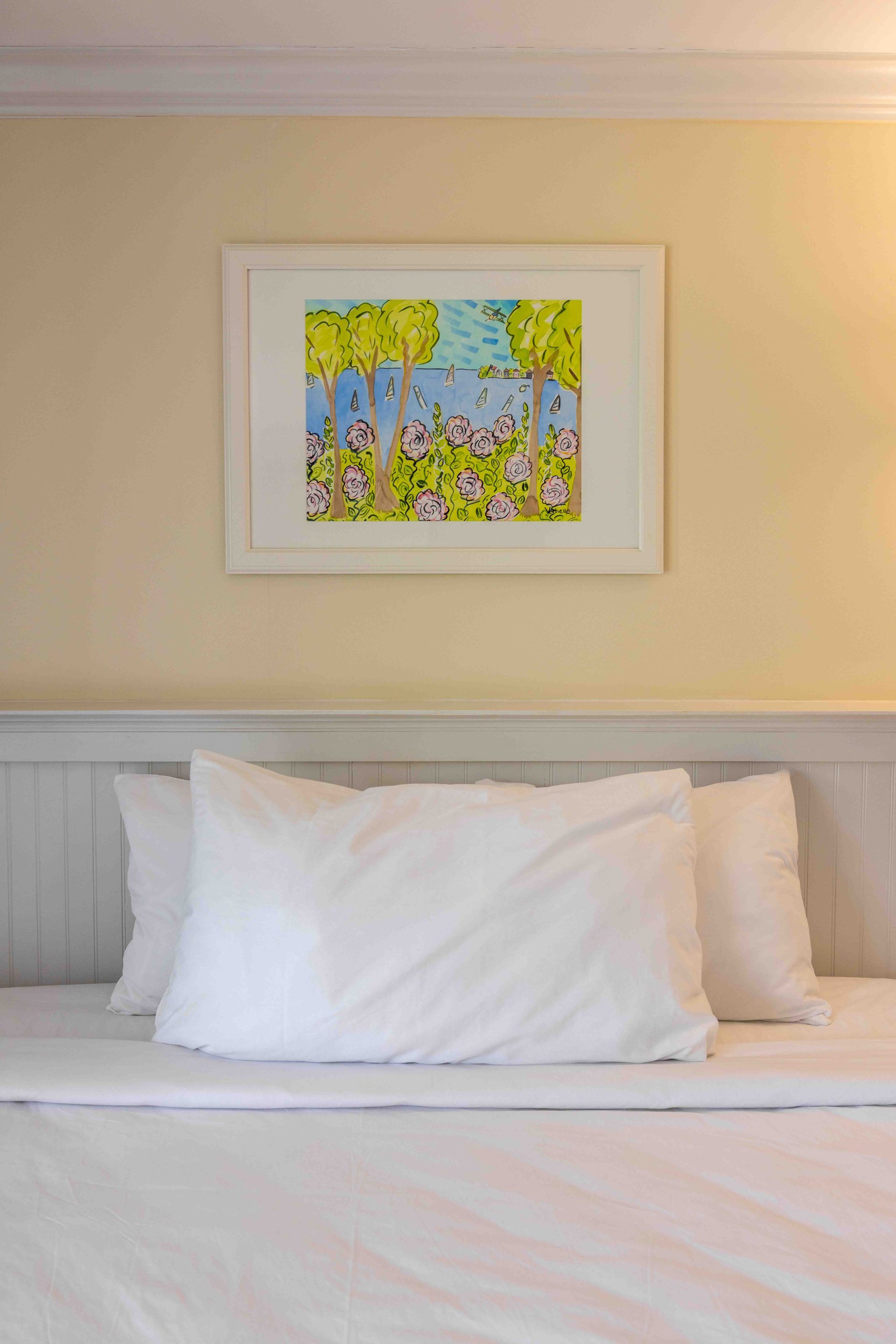 Neatly made bed beneath a framed colorful artwork on a beige wall