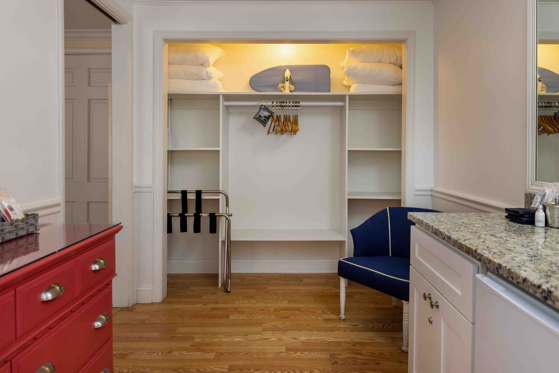 Walk-in closet with white shelves, wood floor, and blue built-in bench beside a bathroom vanity.