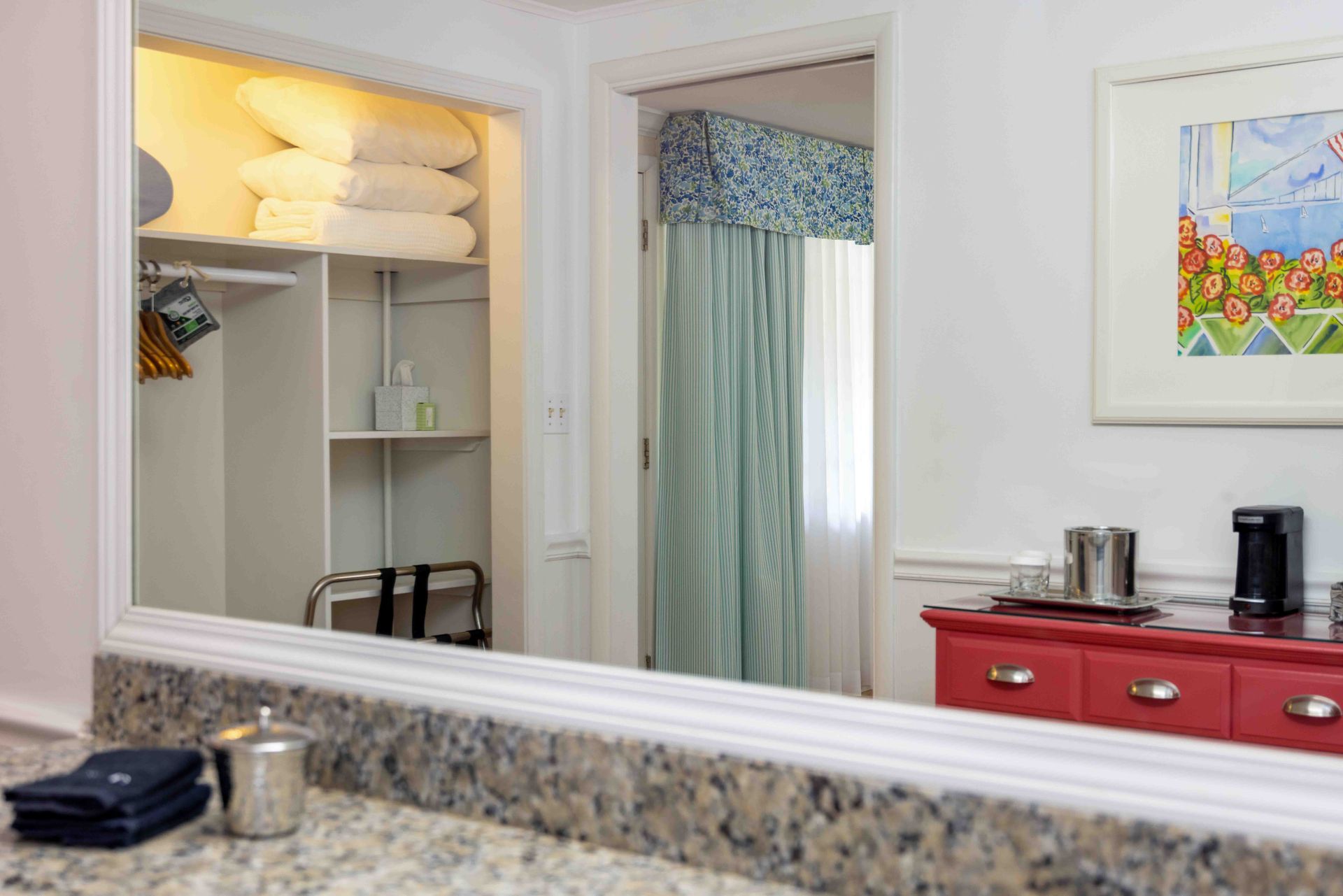 Bathroom vanity and mirror reflecting a closet with towels and a blue curtain beside a red cabinet.