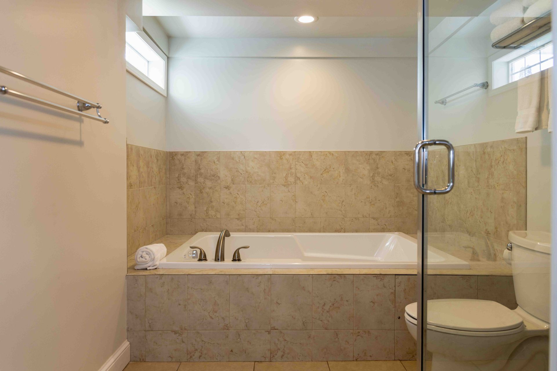Modern beige-tiled bathroom with a built-in bathtub and glass shower enclosure