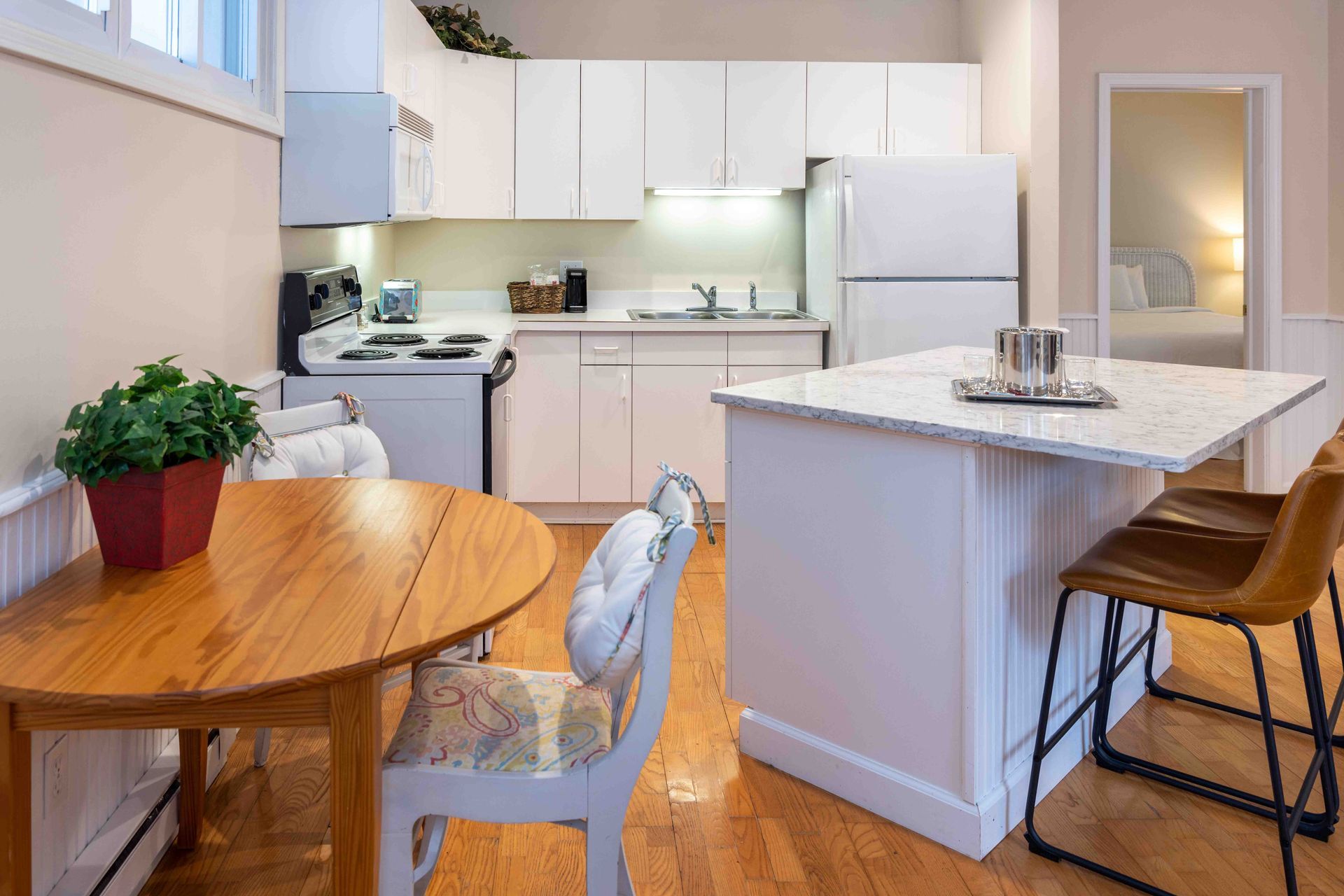 Bright kitchen and dining area with white cabinets, a round wooden table, island, and bar stools
