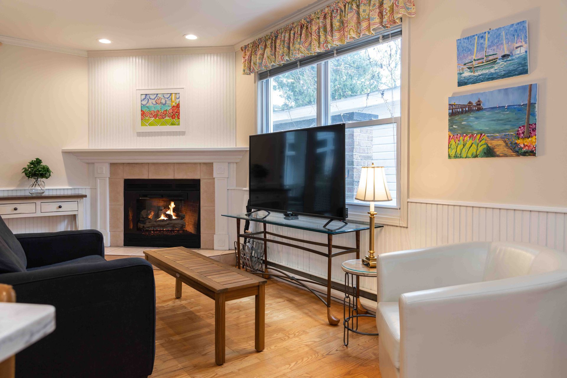 Bright living room with fireplace, large TV, coffee table, and white armchair by a window