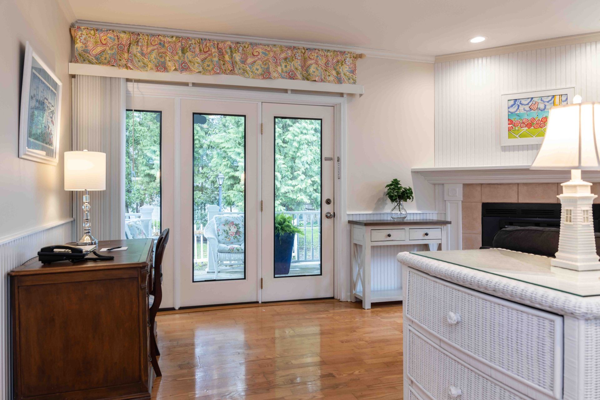 Bright living room with white fireplace, glass doors, wood floor, and floral valance under soft lighting