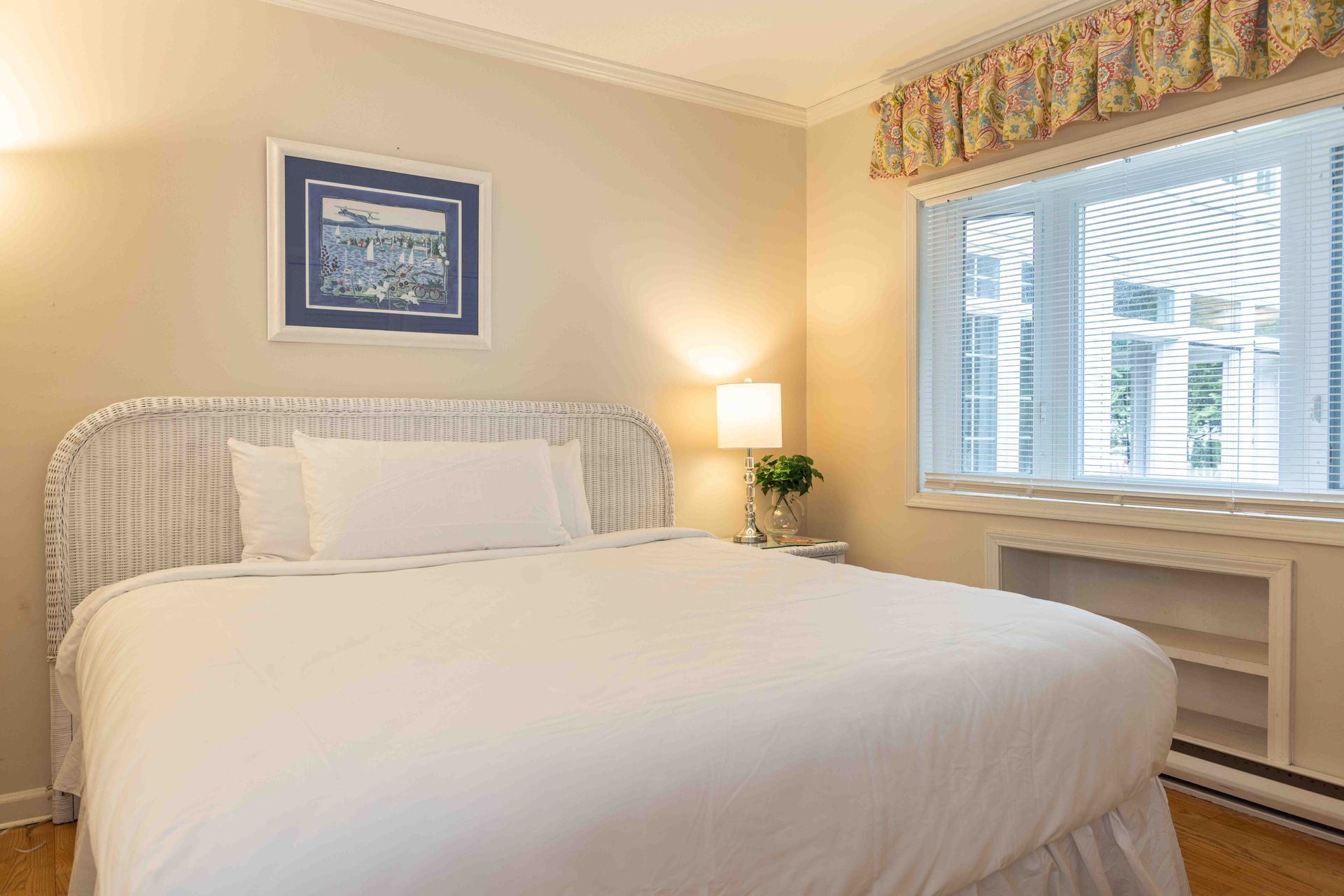 Bright bedroom with a white bed, lamp, window seat, and framed wall art