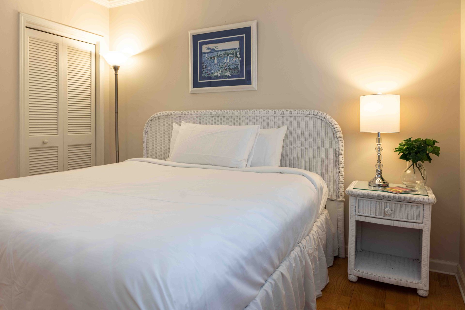 Cozy bedroom with white bed, bedside lamp, framed art, and a potted plant.