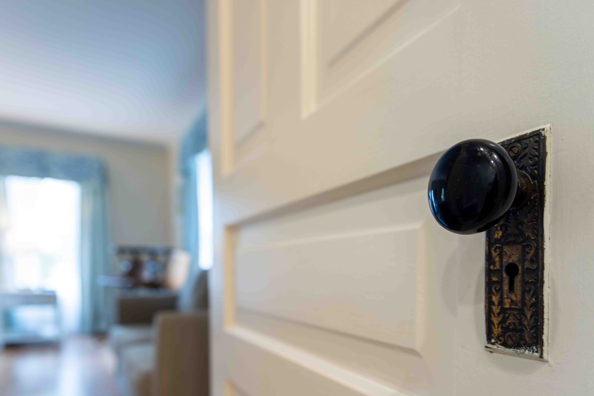 Close-up of a black door knob on a white paneled interior door, with a blurred hallway beyond