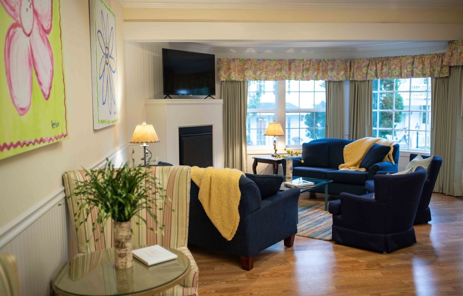 Bright living room with blue chairs, fireplace, large windows, and floral decor