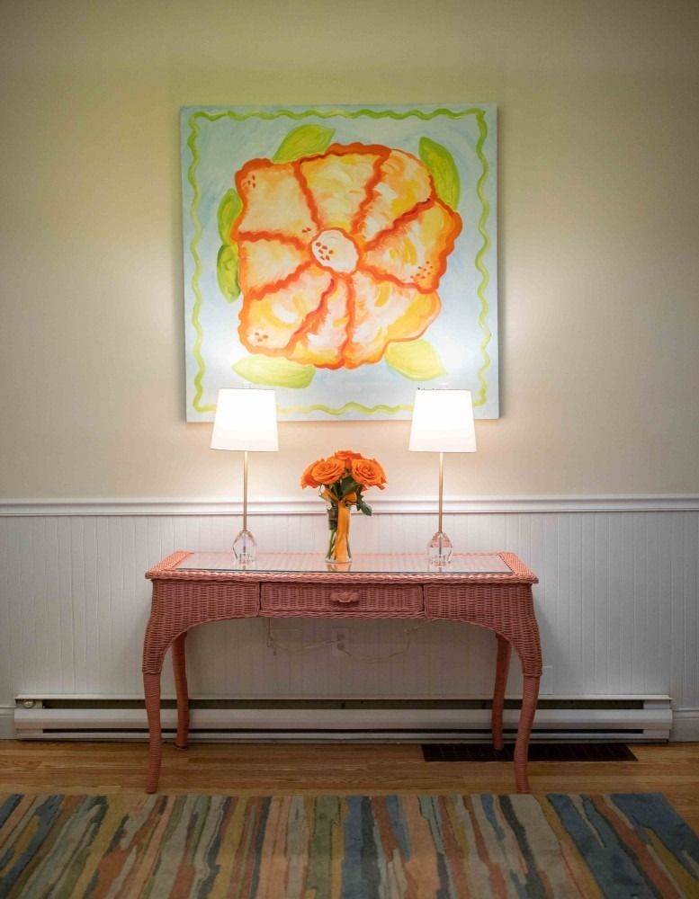 Small table with two lamps and flowers beneath a colorful floral painting in a room