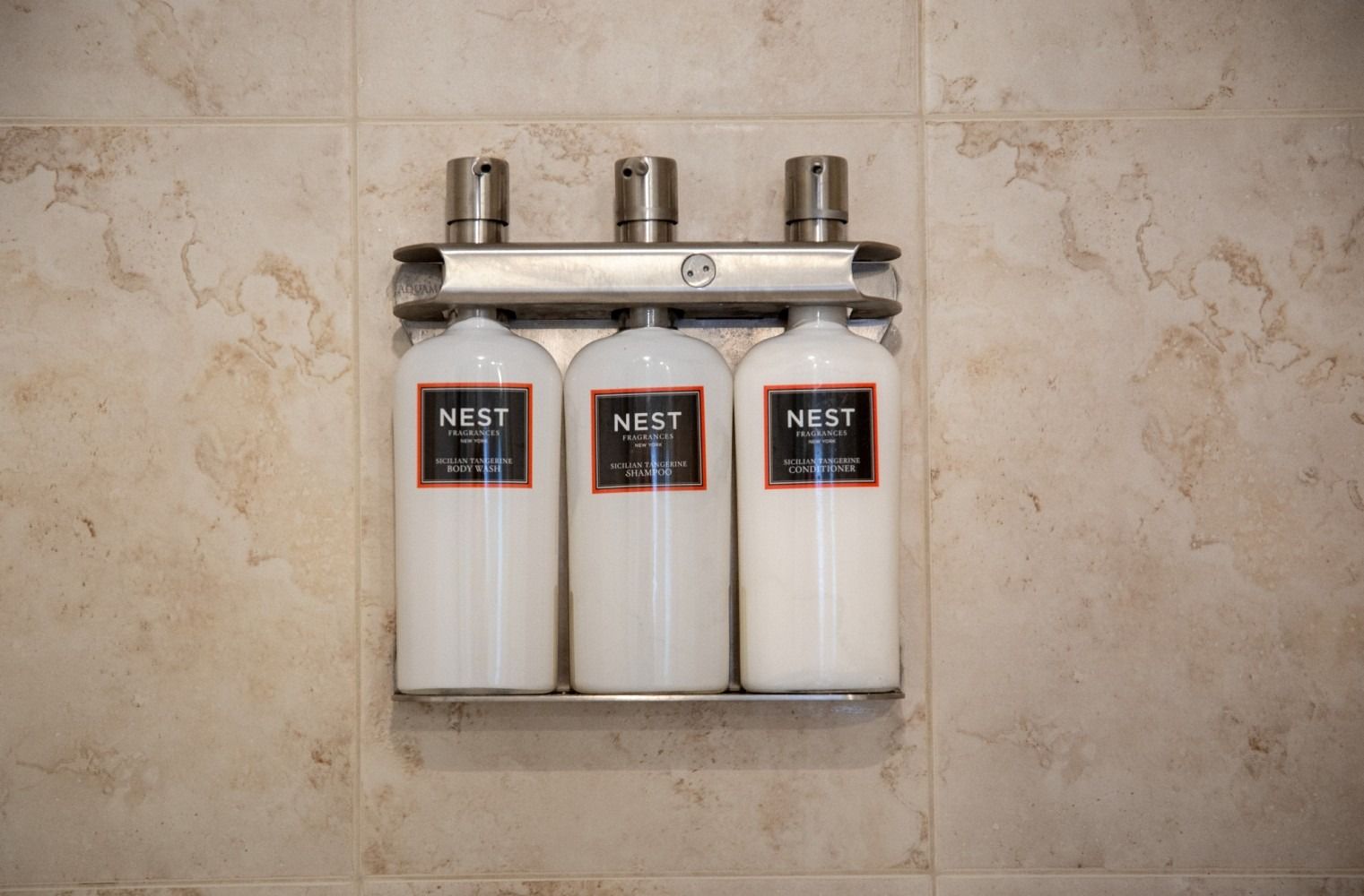 Three Nest bathroom dispensers mounted on a beige tiled wall