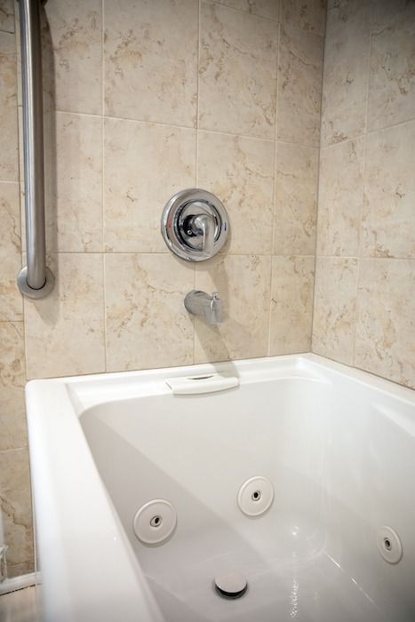 Bathtub and shower in beige tiled bathroom with chrome grab bar and faucet