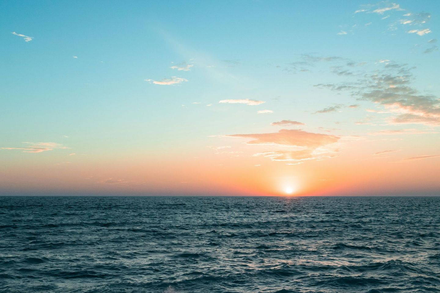 Sunset over a calm ocean, with orange light on the horizon and a pale blue sky.
