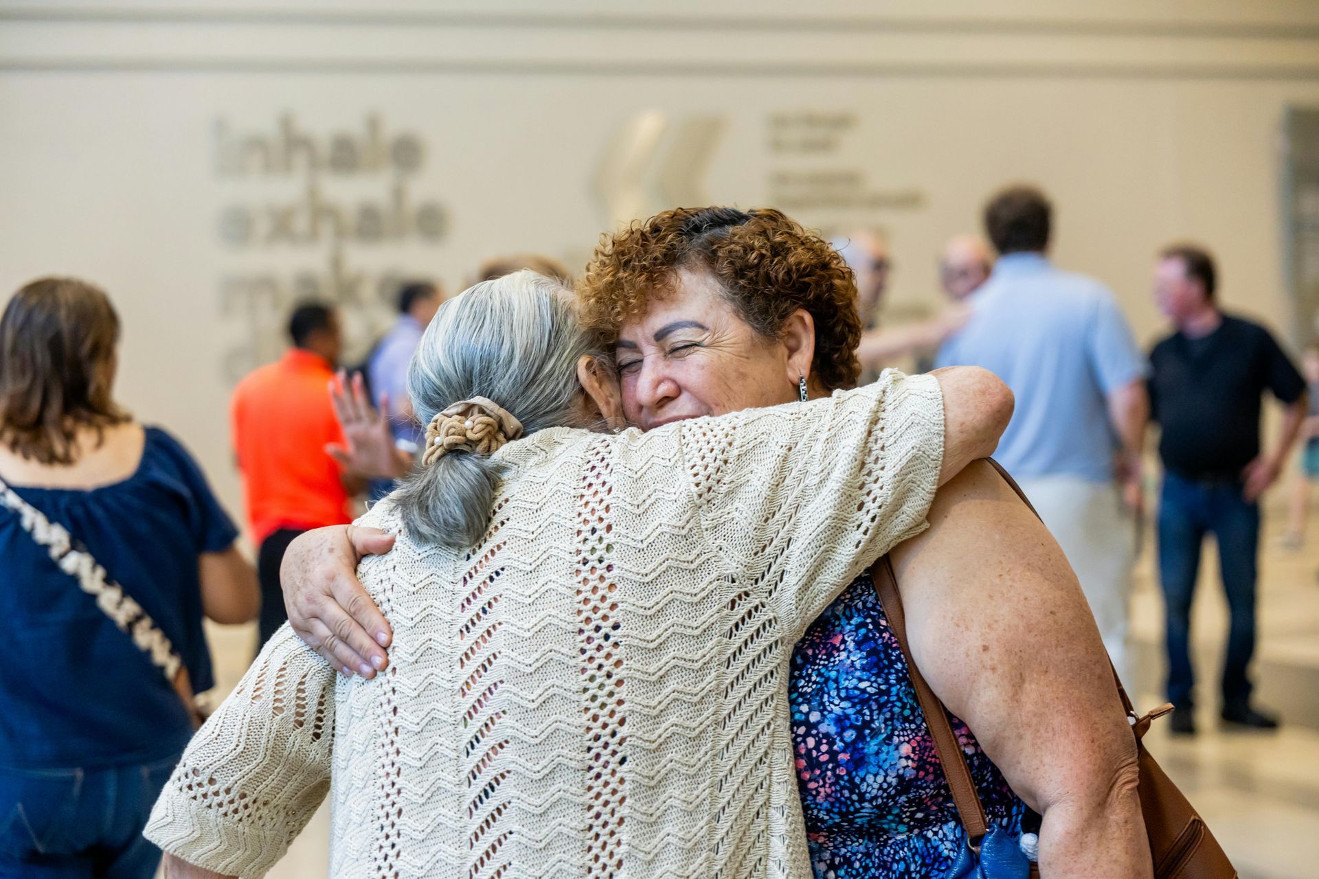 Two people hugging in a bright indoor space with blurred attendees in the background