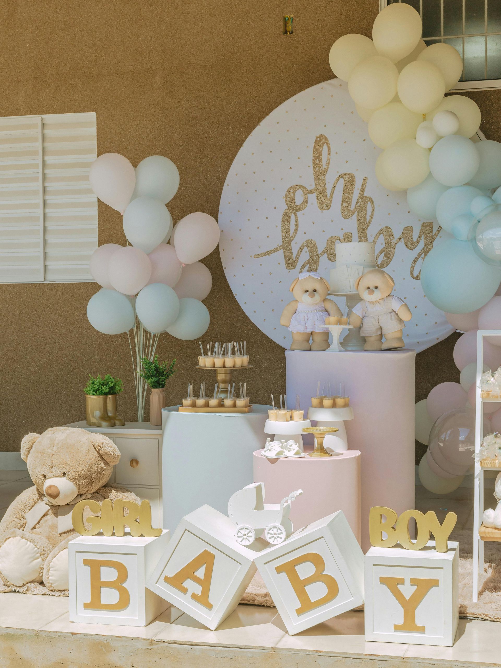 Baby shower dessert table with pastel balloons, teddy bears, and gold “BABY” letters in a white-and-gold setup