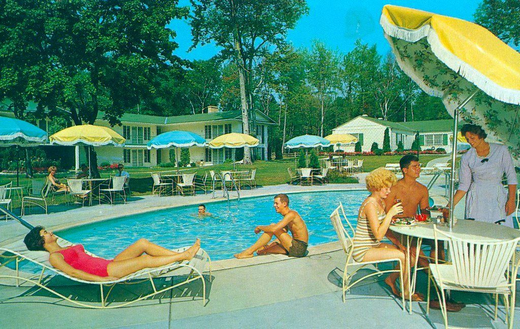 People lounging by a blue swimming pool with yellow umbrellas and lounge chairs