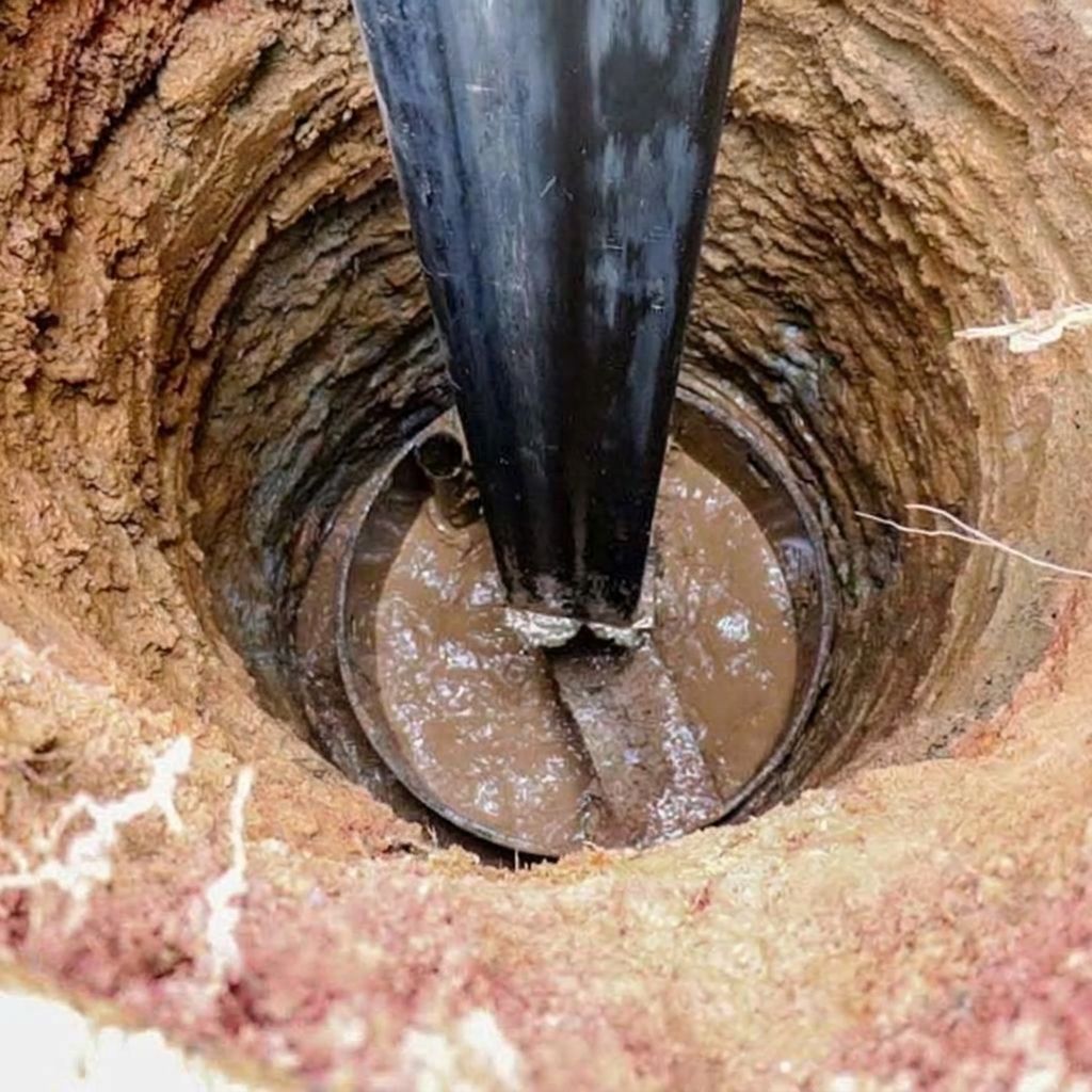 Cavo nero che scende in un buco circolare fangoso o in un pozzo, con terreno bagnato intorno al bordo