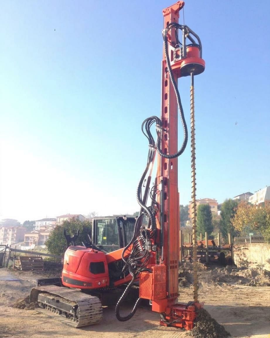 Impianto di perforazione rosso cingolato in un cantiere, sotto un cielo azzurro terso.