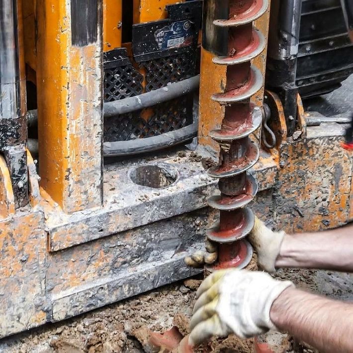 Un operaio stringe una punta da trapano arrugginita su un macchinario da cantiere infangato