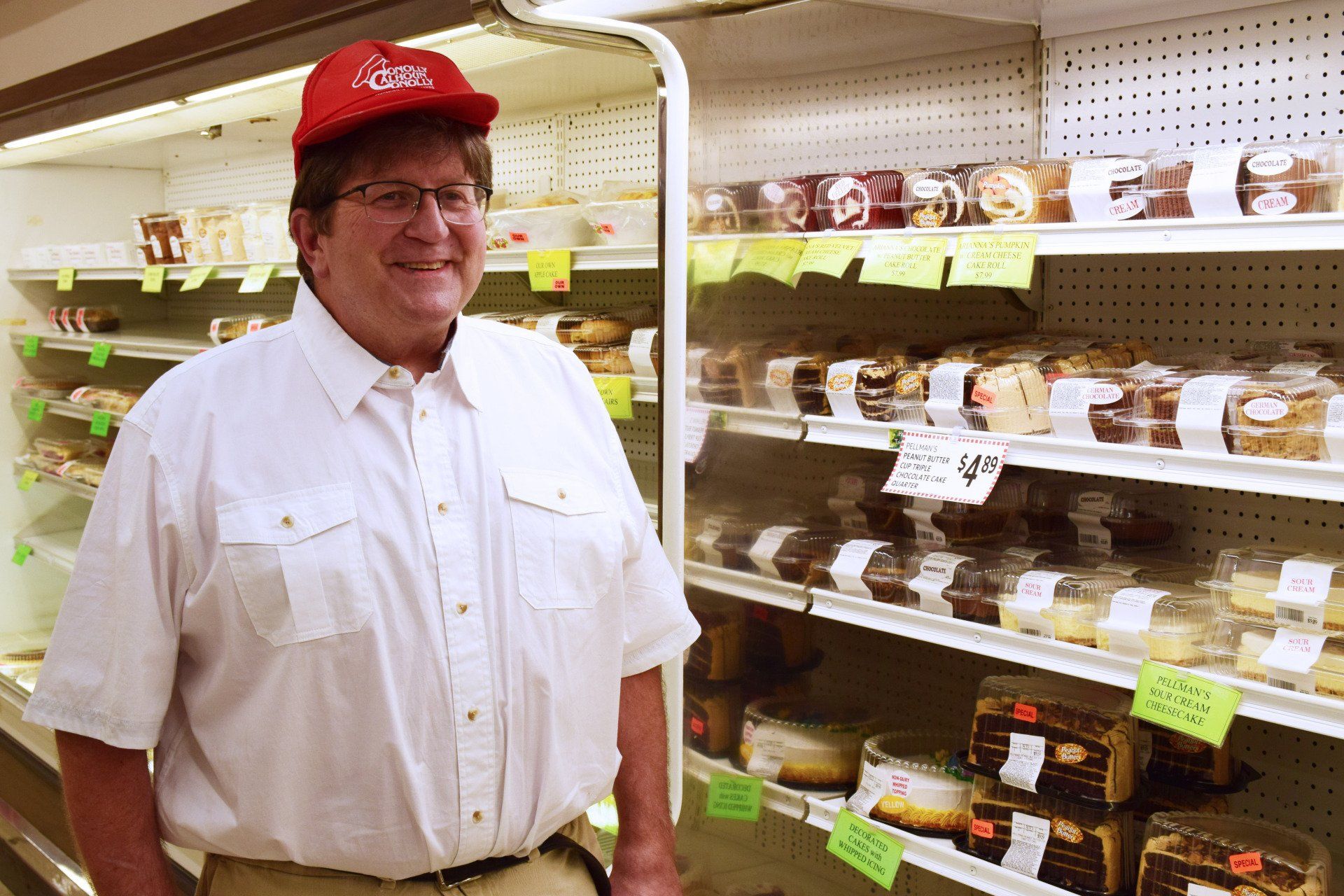 A man wearing a red hat is standing in front of a refrigerator filled with food