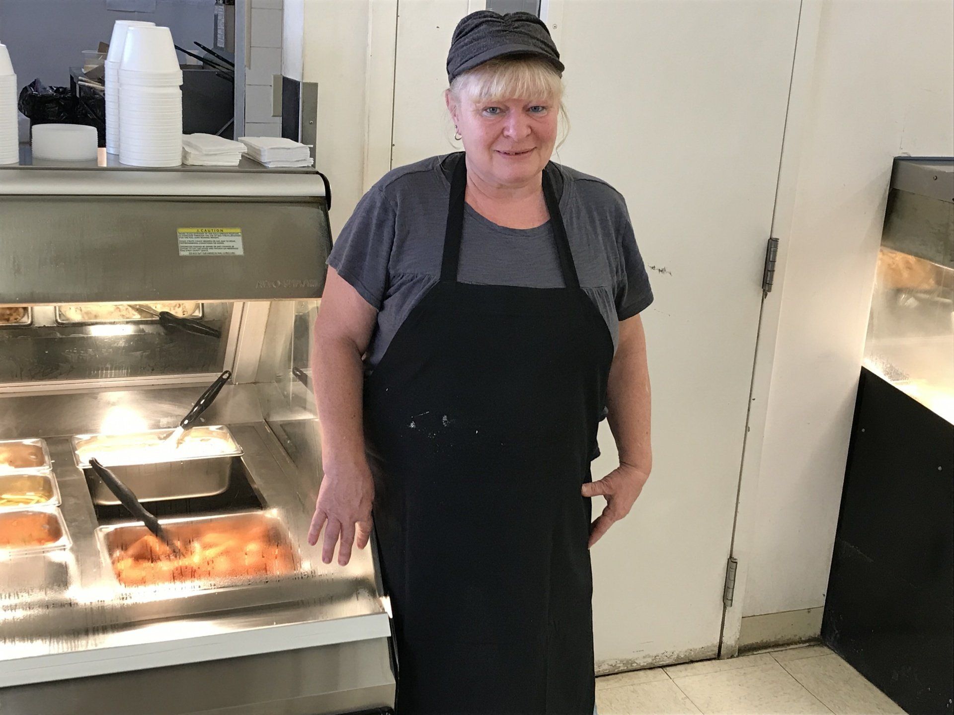 A woman in an apron is standing in front of a buffet line.