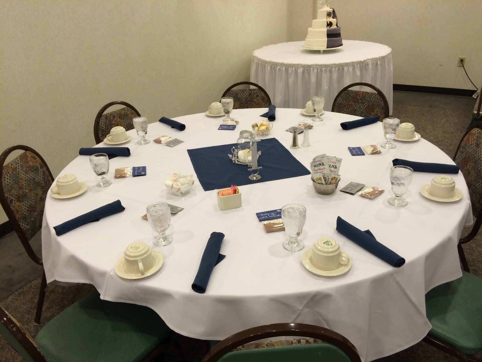 A round table with a white table cloth and blue napkins