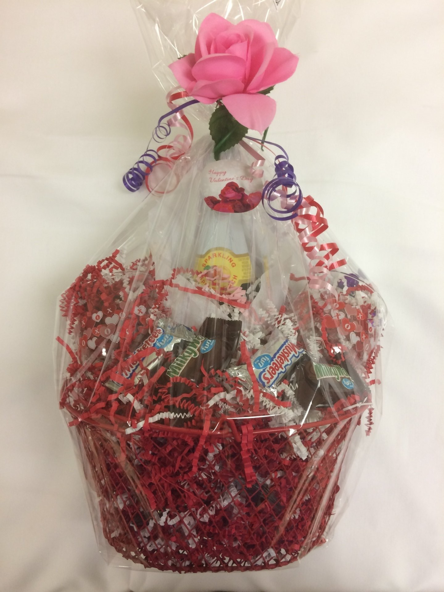 A gift basket filled with candy and a pink rose.