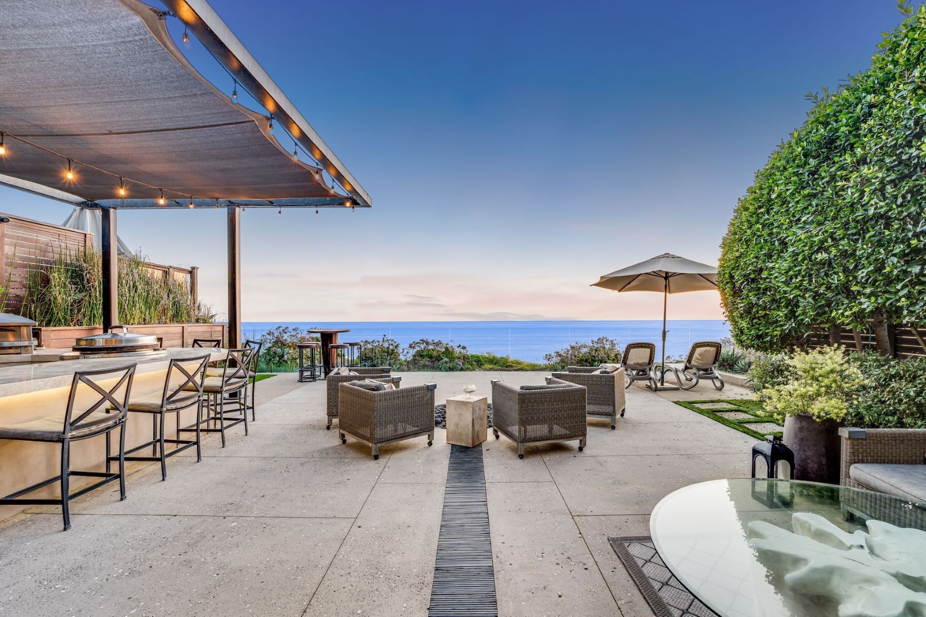 A sunset patio overlooking the ocean with a covered outdoor kitchen, bar stools, and casual seating area.
