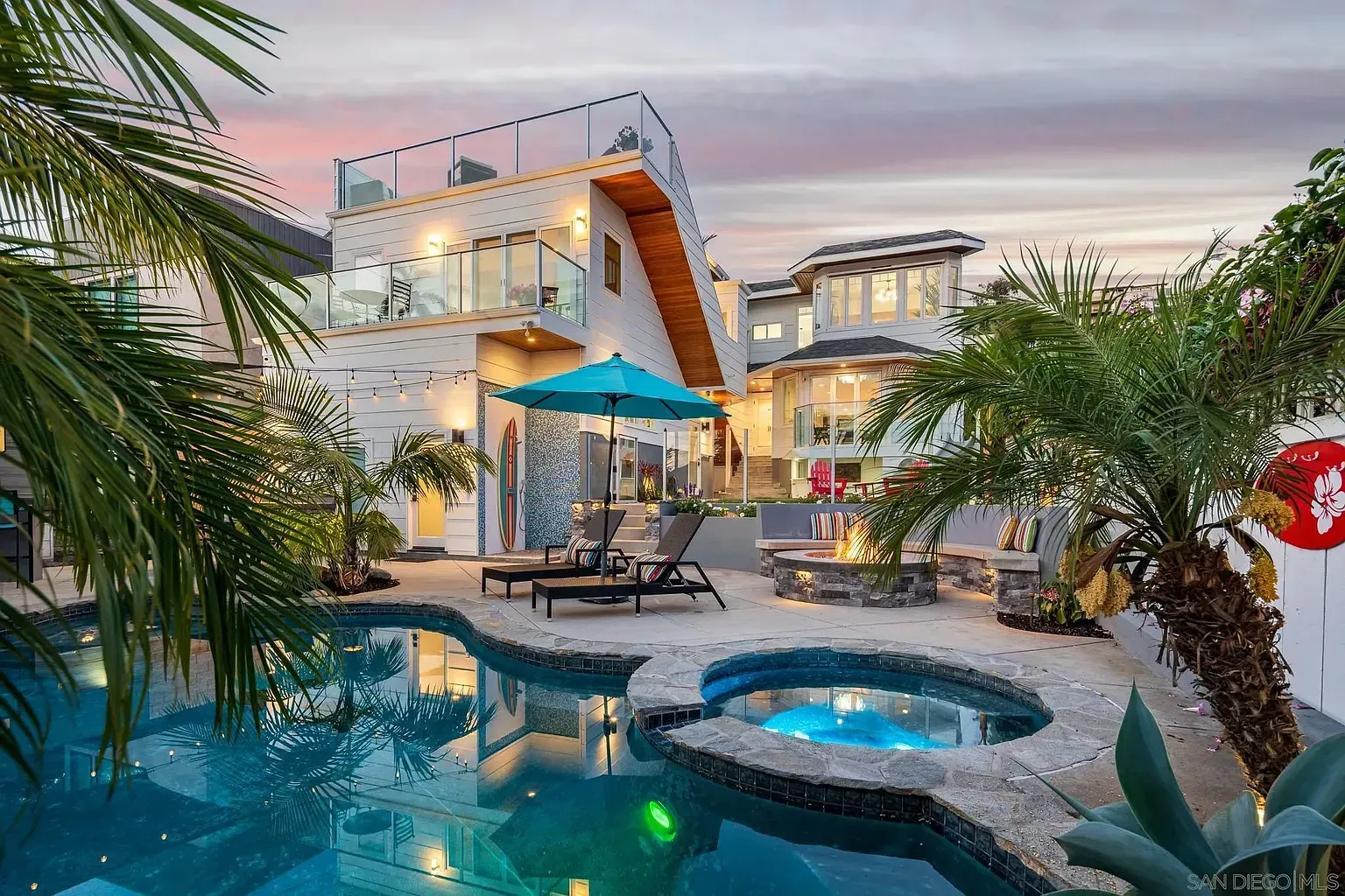 A luxury home with a swimming pool, hot tub, patio furniture, and a fire pit at sunset.