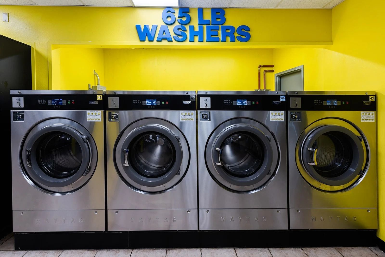 Four large washing machines in a yellow laundromat; text above says 