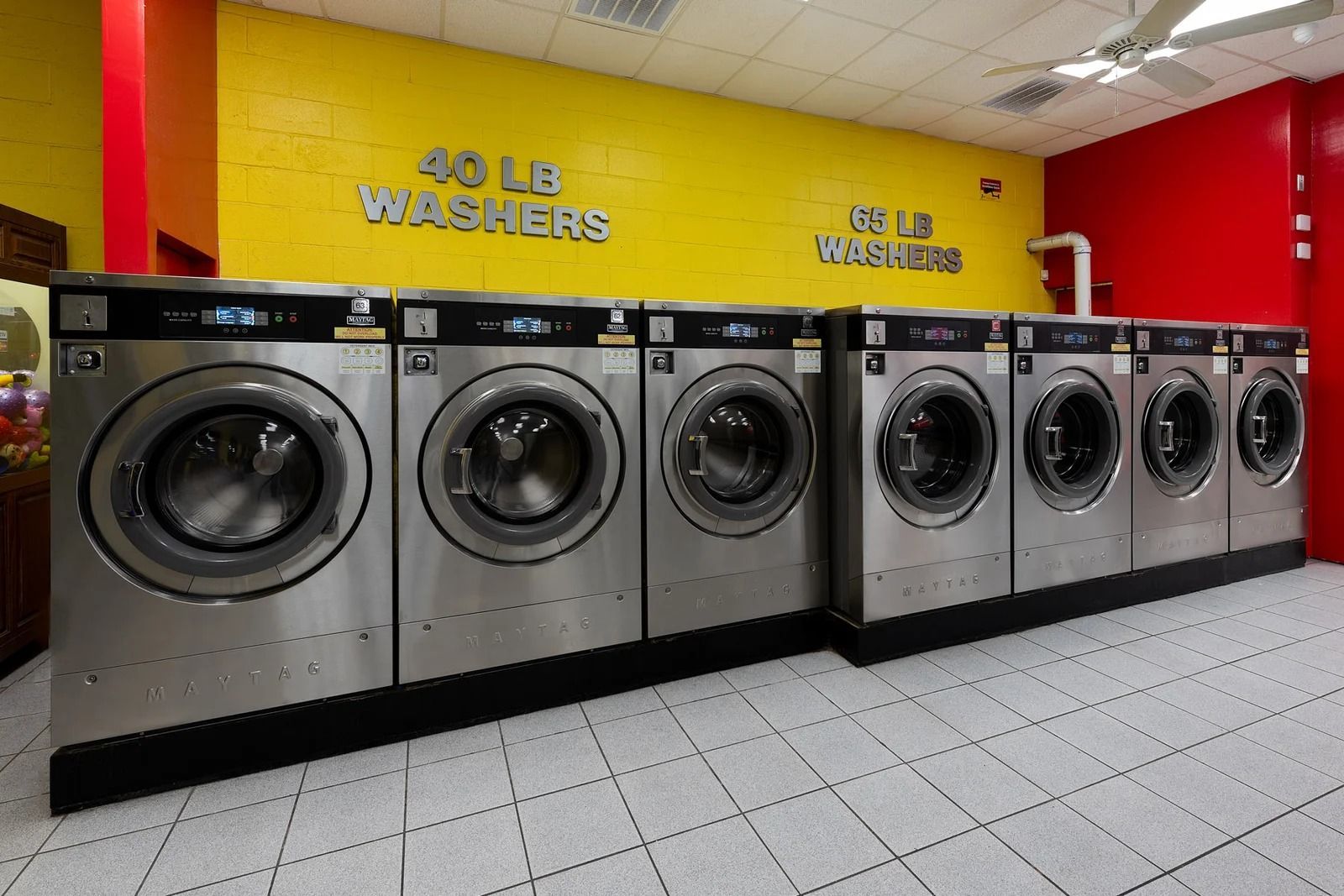 Row of washing machines in a laundromat, against yellow and red walls.